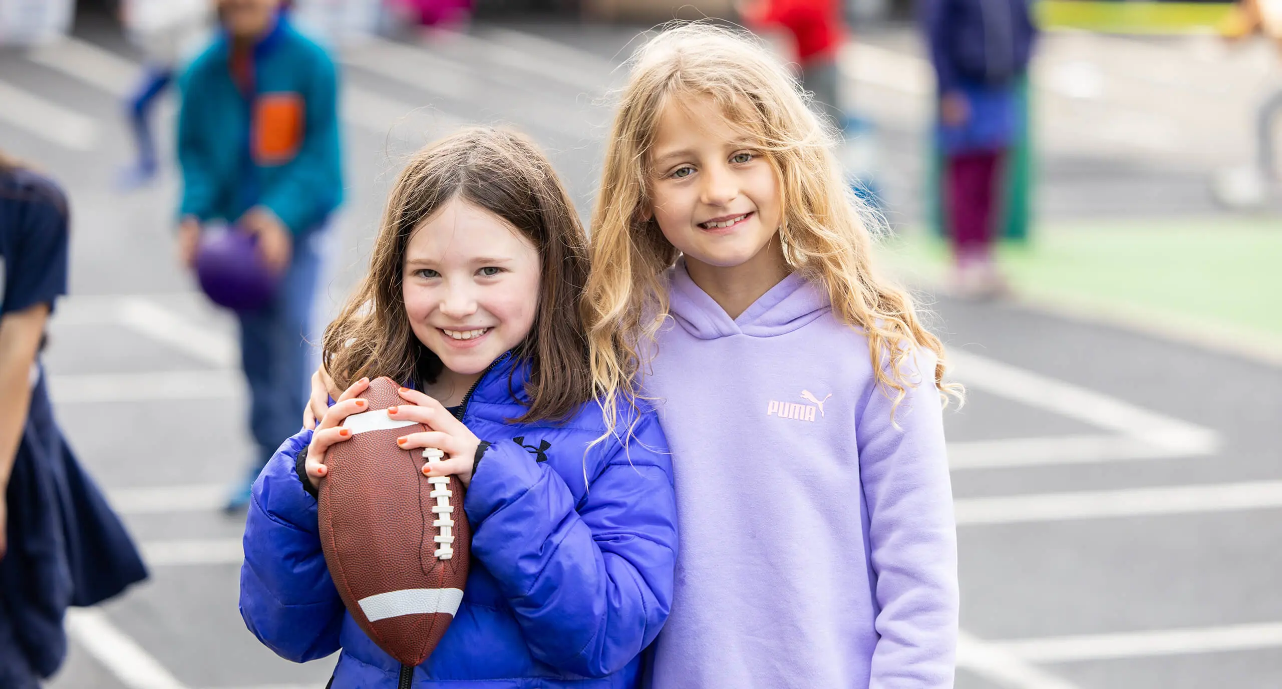 two girls on a playground, one with a football