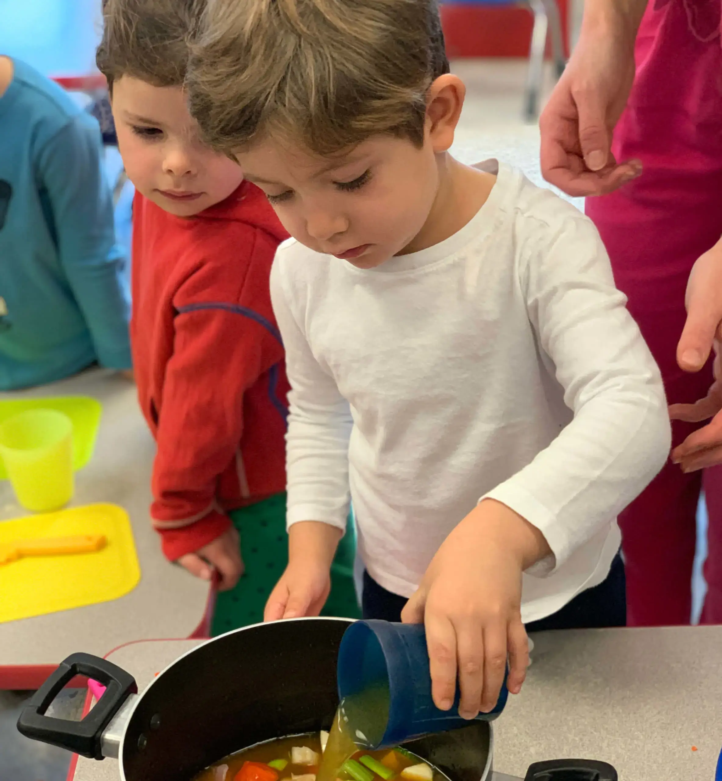 small child adding broth to a pot