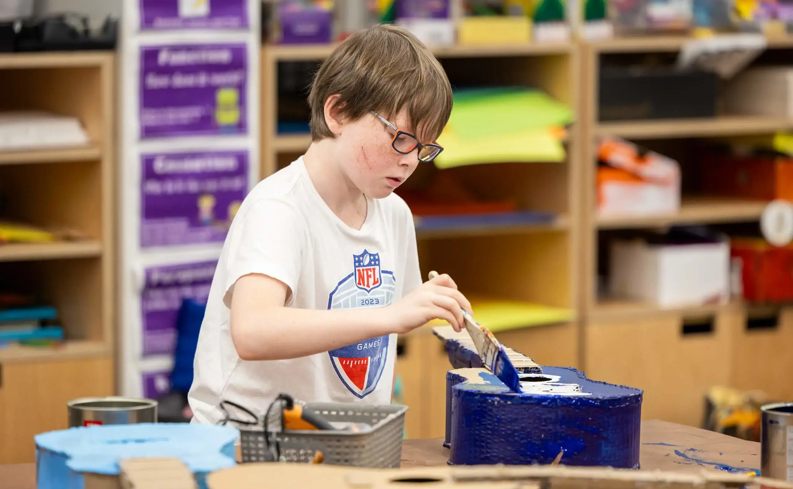 Student with glasses painting a guitar dark blue